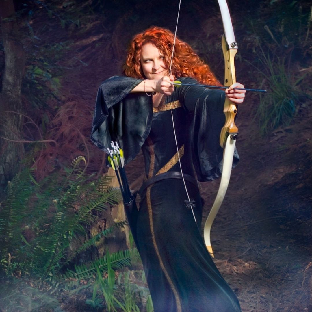 jessicurl founder, Jess McGuinty, dressed as Merida from Brave in a green dress and bow standing in a forest