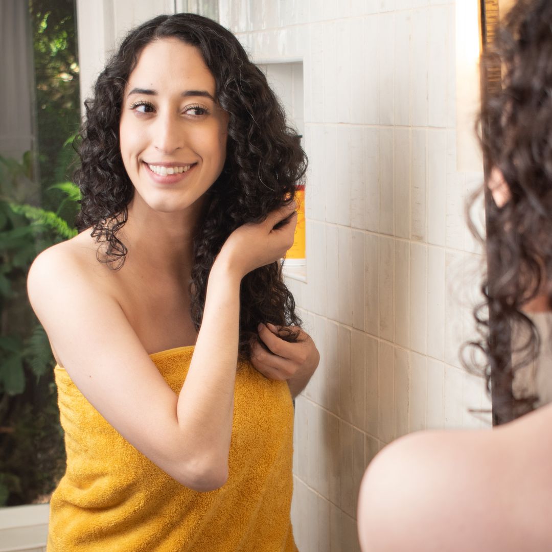 curly haired woman applying Jessicurl Spiralicious Styling Gel to her hair after her shower to create a cast