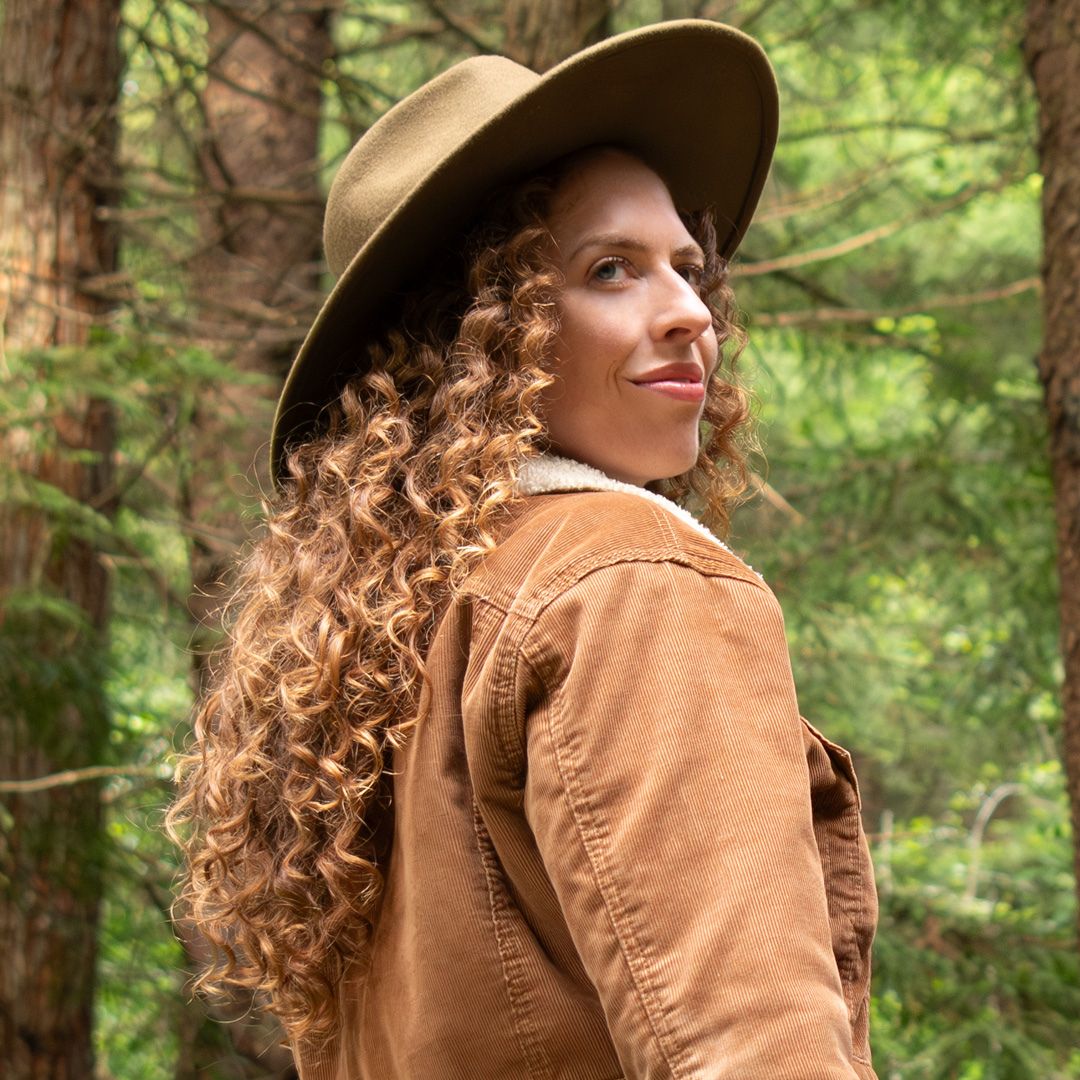 curly haired woman looking over her should past the camera while walking in the woods