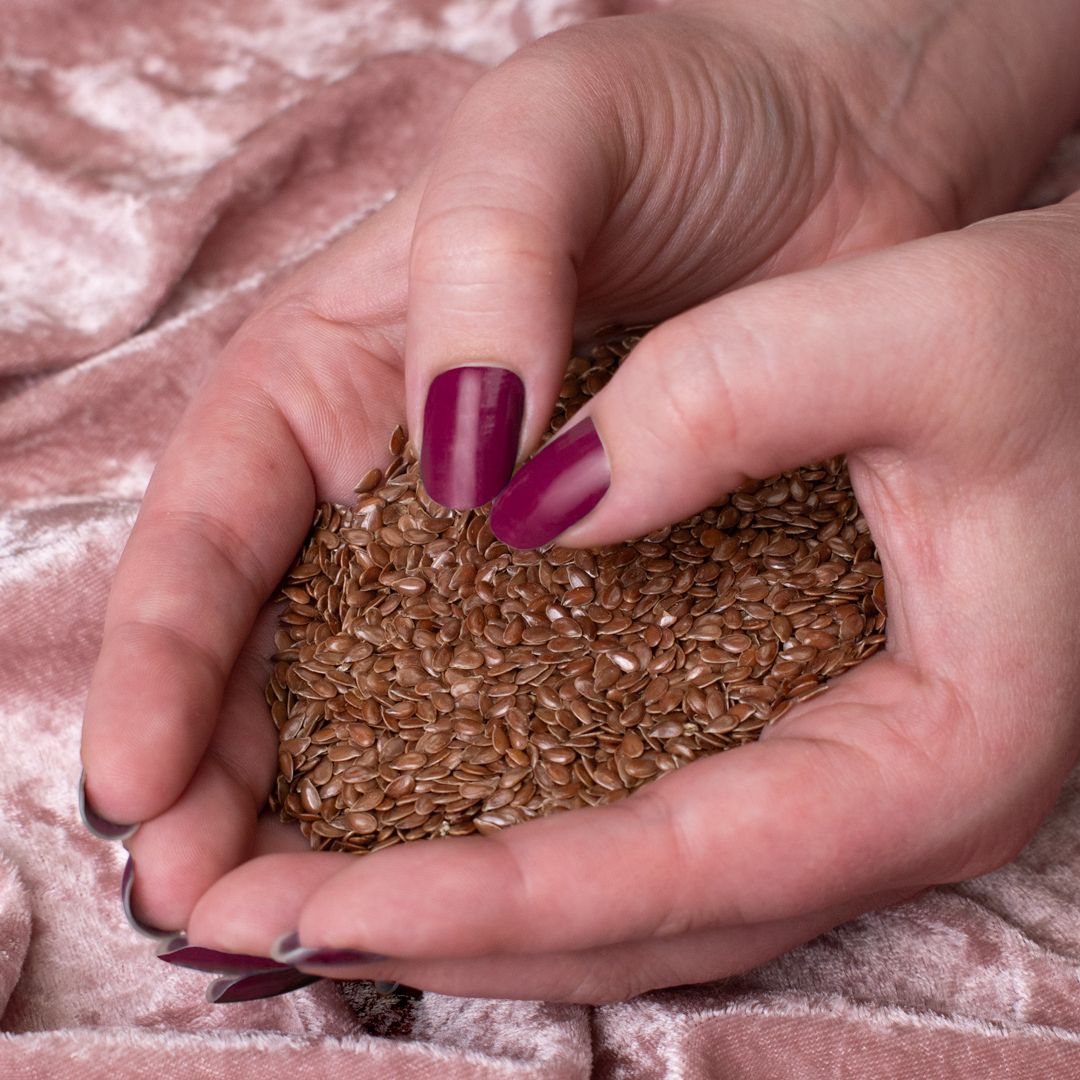 hands forming a heart shape as they hold flax seeds on top of pink fabric