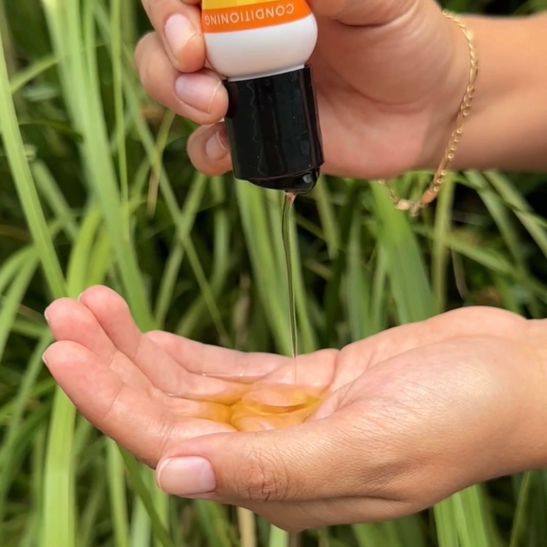 person pouring Jessicurl Oil Blend into their hand near greenery