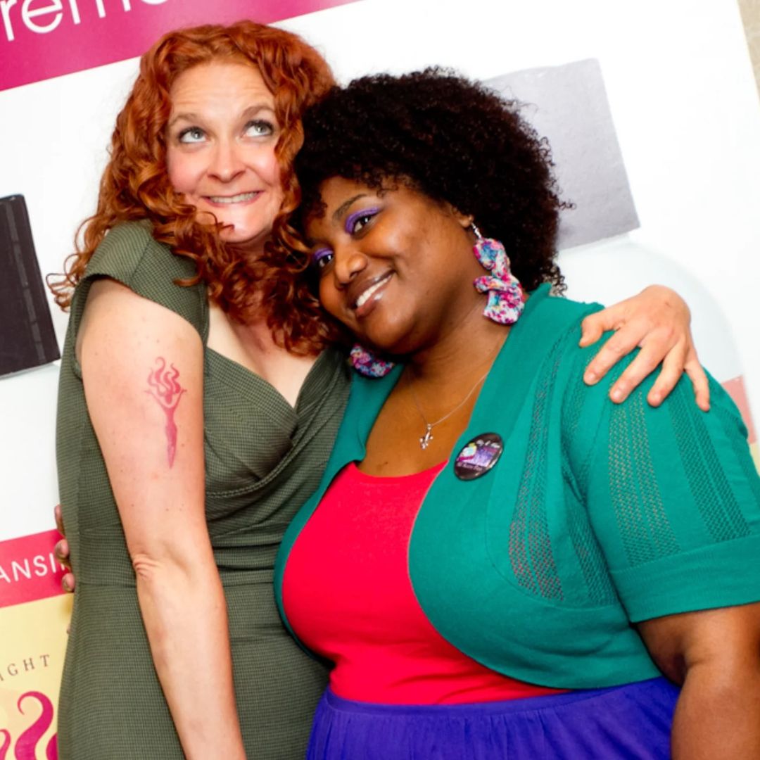 Jessica McGuinty with Haley Rhine hugging and smiling for the camera in front of a Jessicurl poster