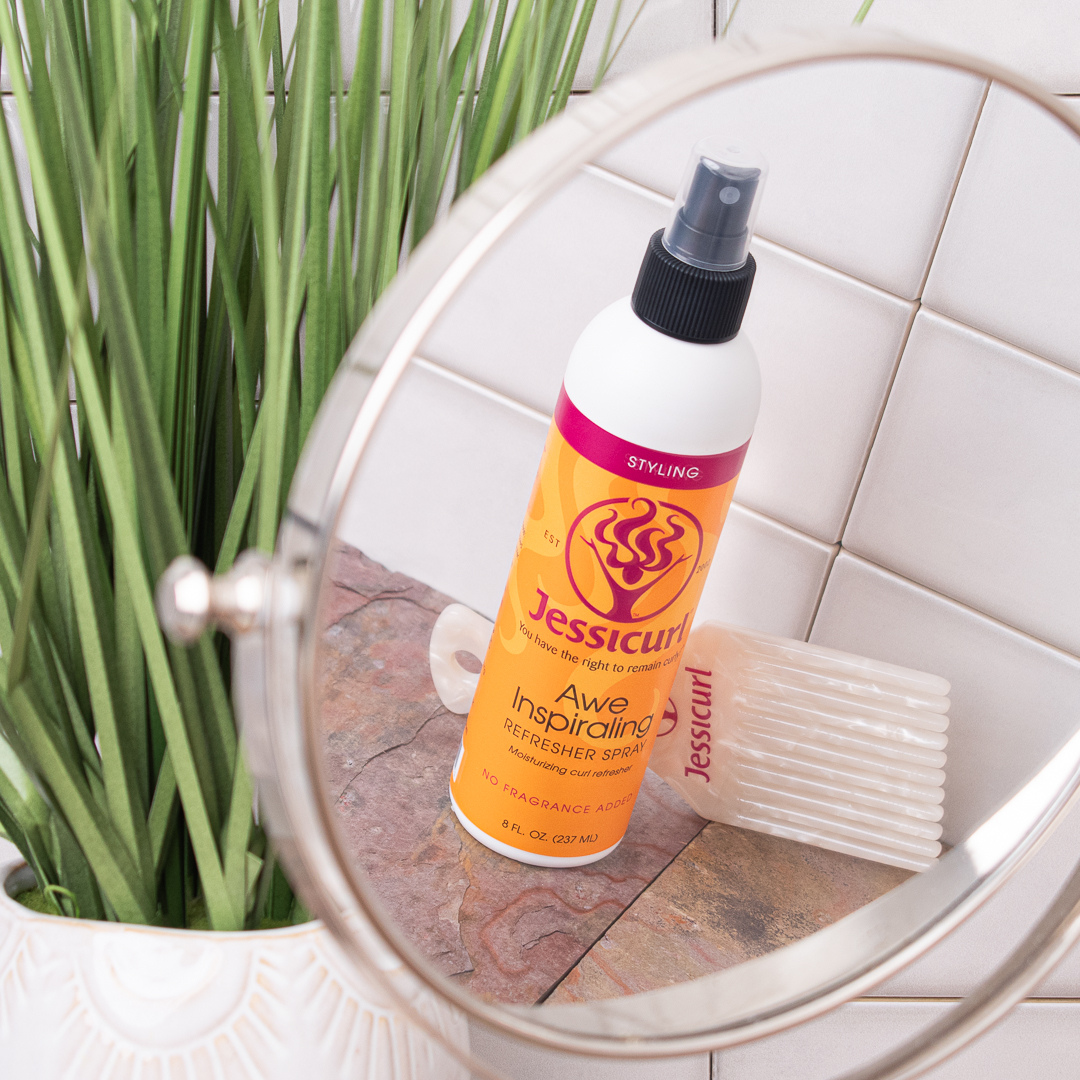 Jessicurl's Awe Inspiraling Refresher Spray and a Jessicurl pearl pick comb reflecting in a small mirror on the bathroom counter