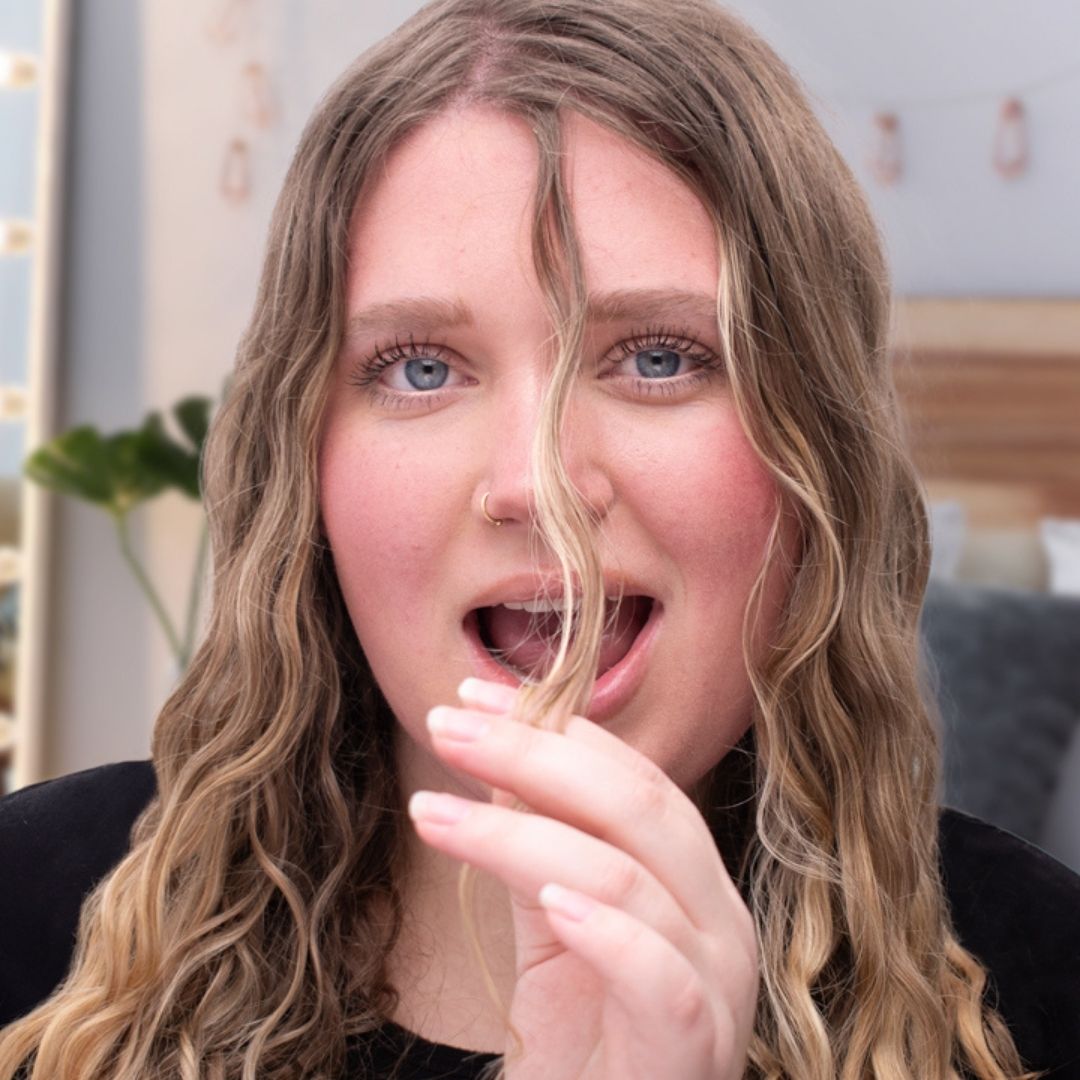 Girl in bedroom with hair strand in front of face making a happy open-mouthed expression