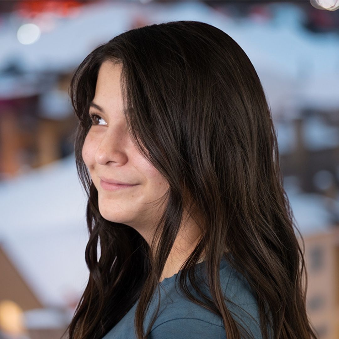 woman with brown, wavy hair looking off camera with a snowy town hazily behind her