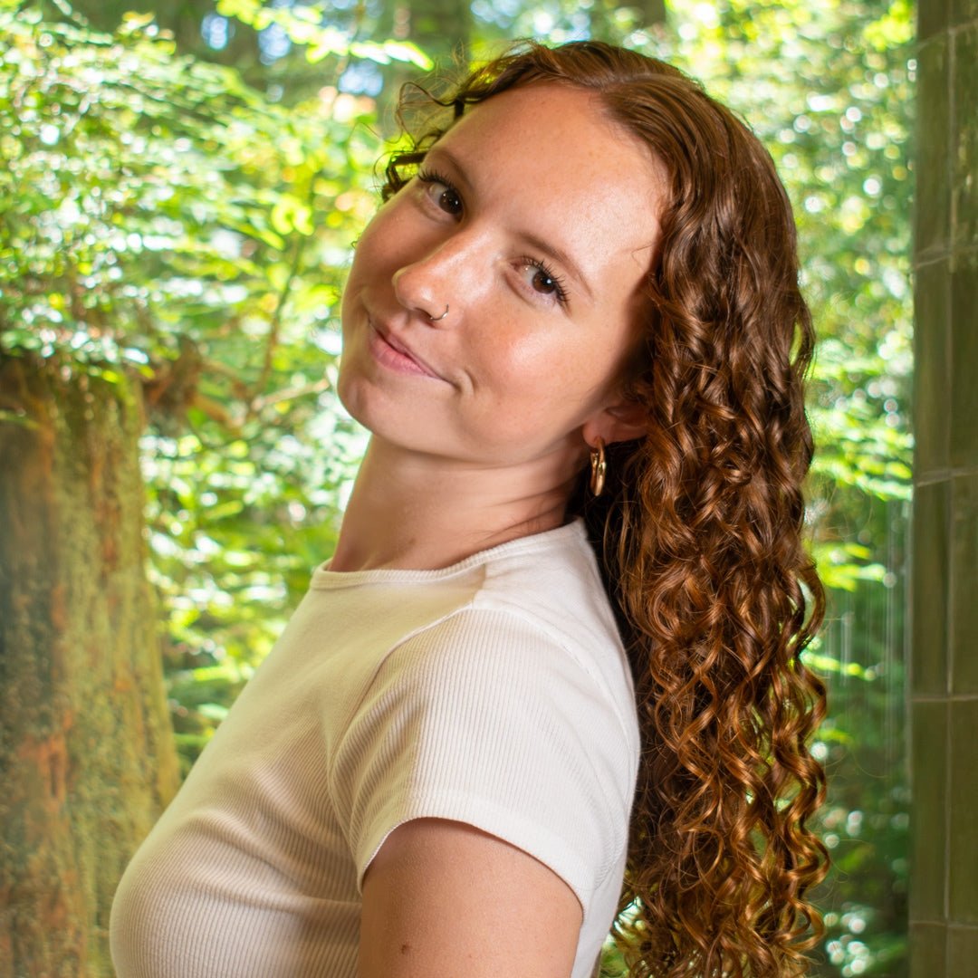 a curly haired woman smiling at the camera as she leans back to show off her long curls