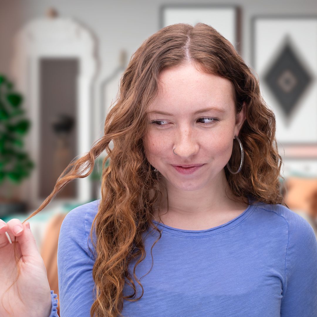 wavy haired woman smiling shyly as she twirls a lock of hair in her fingers