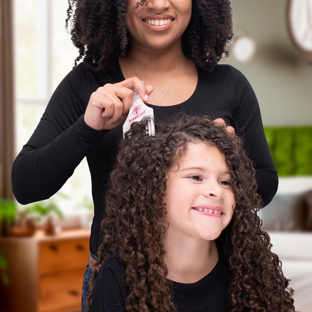 a coily haired mother with her curly haired daughter sitting in front of her as the mother uses a Jessicurl Hair Pick to refresh her daughter's hair