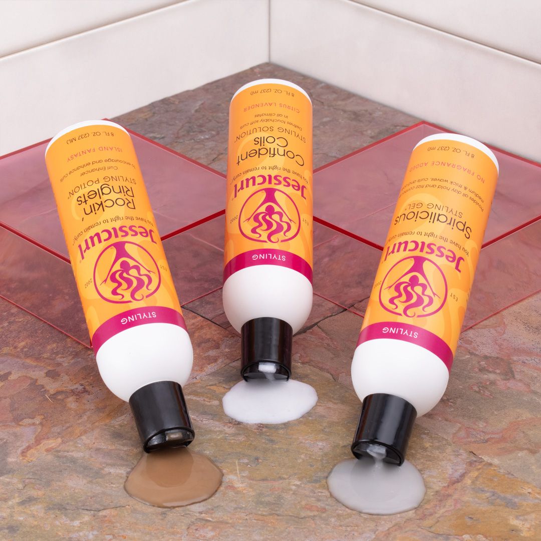 Jessicurl Rockin Ringlets Styling Potion, Confident Coils Styling Solution, and Spiralicious Styling Gel laying on their sides on a granite counter spilling the product out of the top