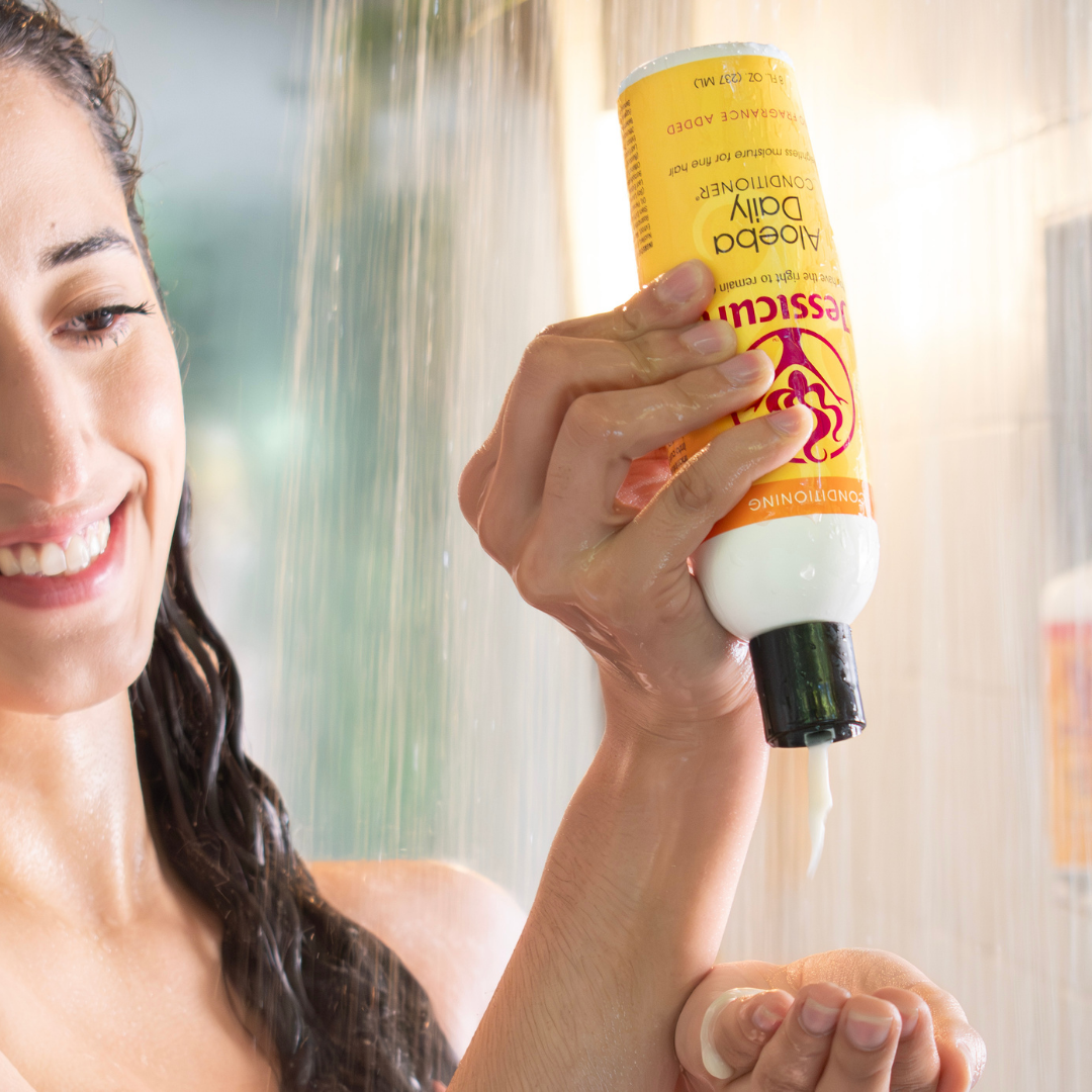 curly haired woman in the showedr pouring Jessicurl Aloeba Daily Conditioner into her hand to use