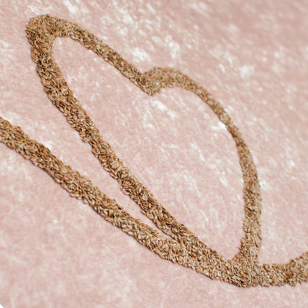 Flaxseeds in a trailing heart formation on a light pink velvety backdrop