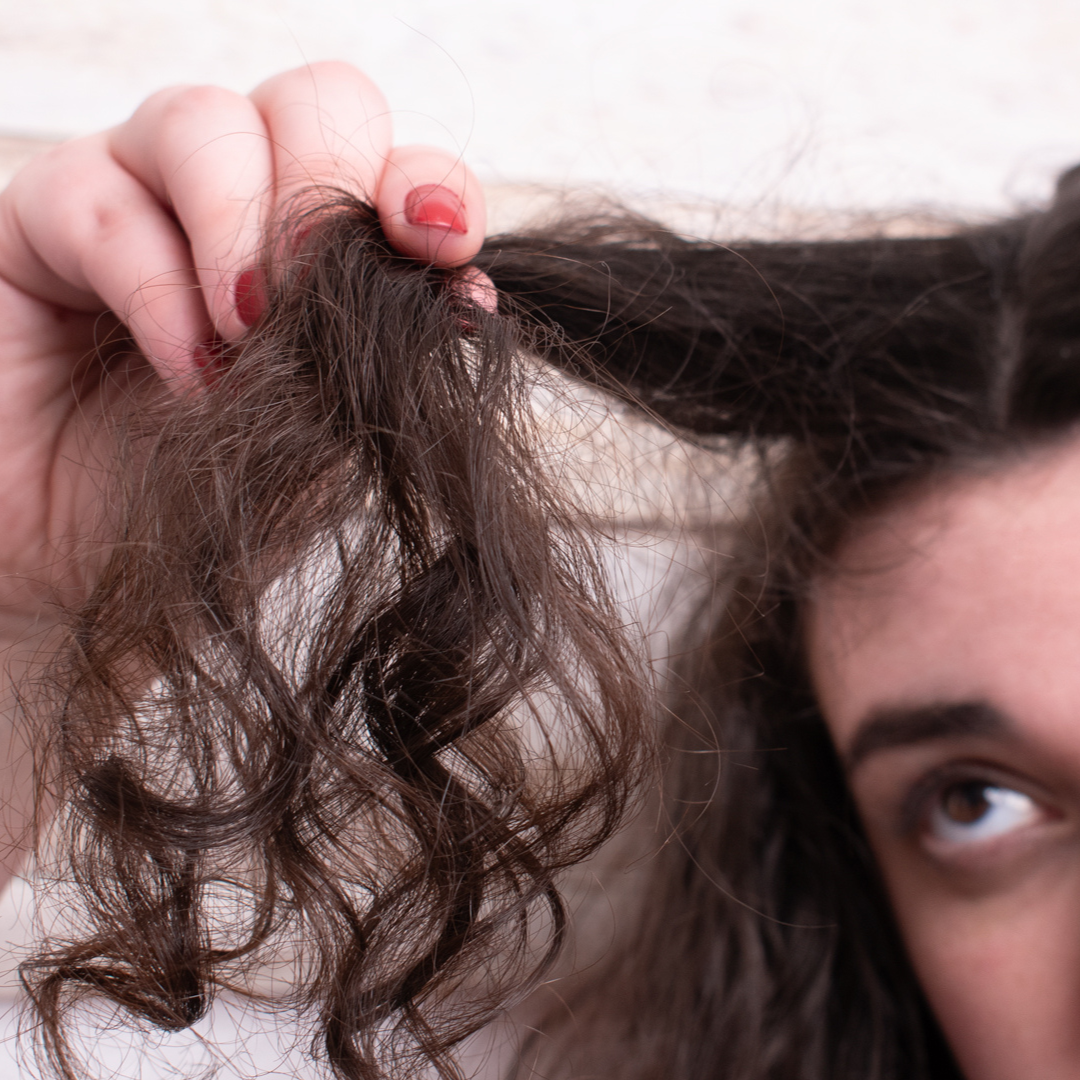 curly haired woman holding a chunk of her hair out to see if she is in the midst of a protein overload