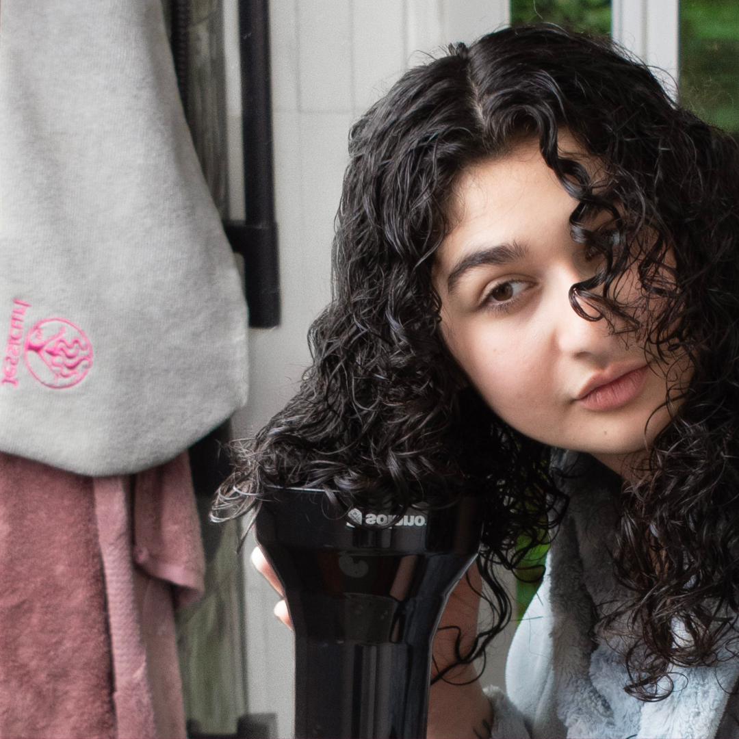 Curly girl diffusing her hair after the shower in the bathroom