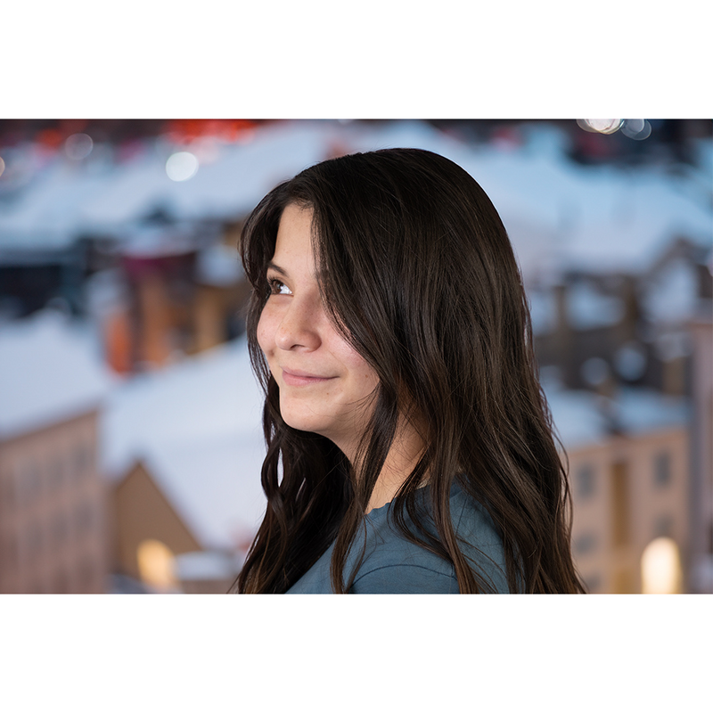 woman with brown, wavy hair looking off camera with a snowy town hazily behind her