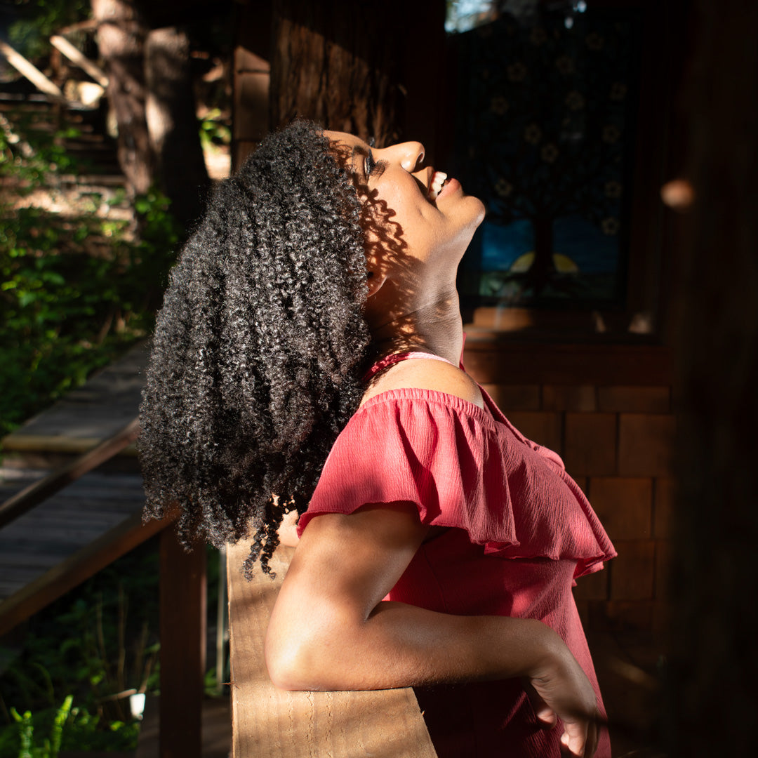 curly haired woman leaning on a wooden rail looking up at the sky with dappled sunlight on her face