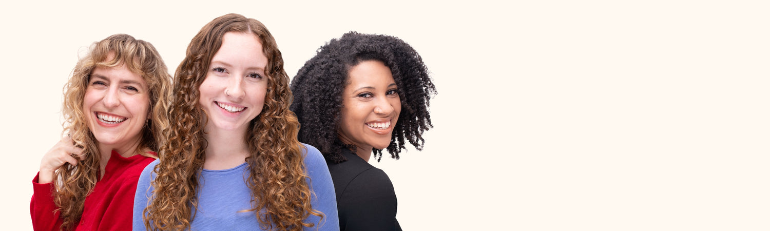 Three women (one with wavy, one with curly, and one with coily hair) smiling.