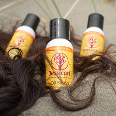 3 bottles of Oil Blend placed in the sand with the ends of curly hair falling around.